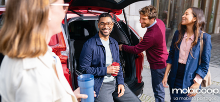Four colleagues looking happy, stood next to a car