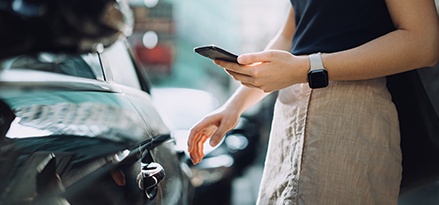 Une personne qui utilise son téléphone tout en ouvrant la portière d’une voiture.